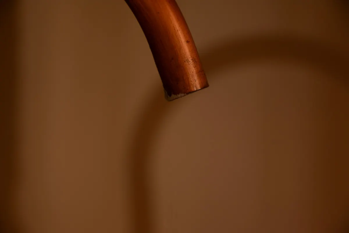 A copper spout curving out of a warm, softly lit wall