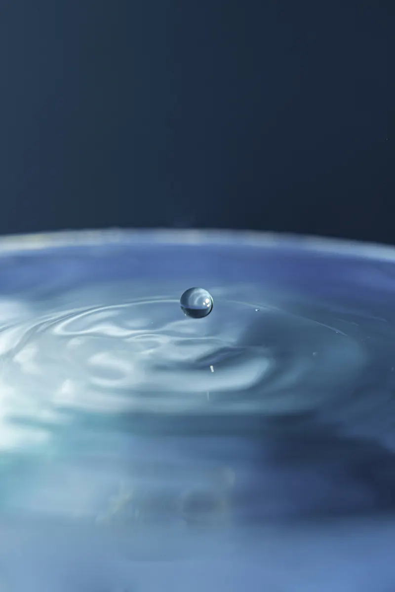 A single drop suspended above rippling blue water