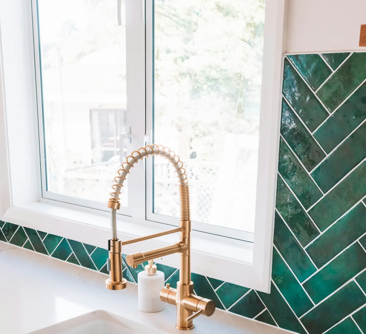 Brass pull-down kitchen faucet with a coiled spring spout in front of green herringbone tile