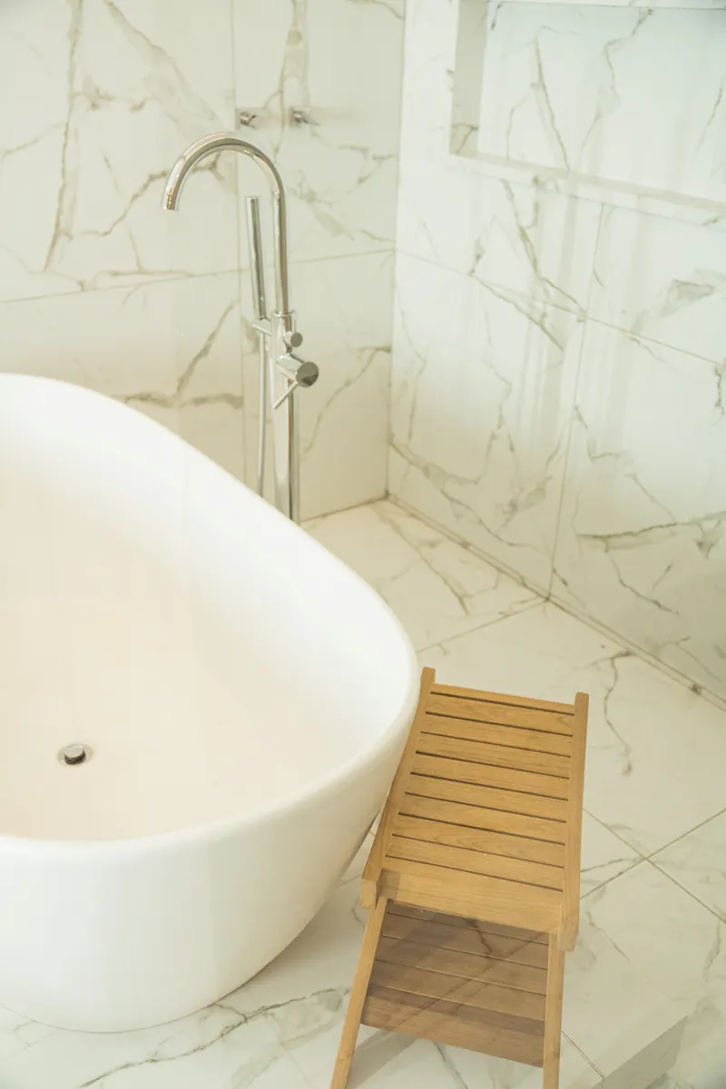 Chrome floor-mounted tub filler beside a white freestanding tub on marble-look tile