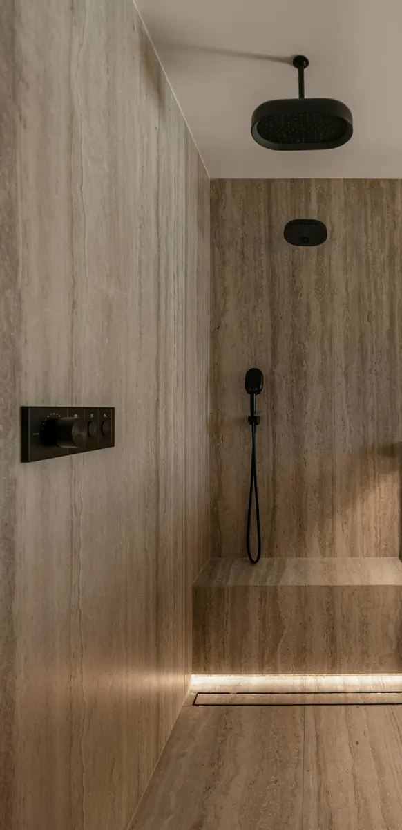 Travertine walk-in shower with a ceiling rain head, a hand shower on a hose and matte black thermostatic controls